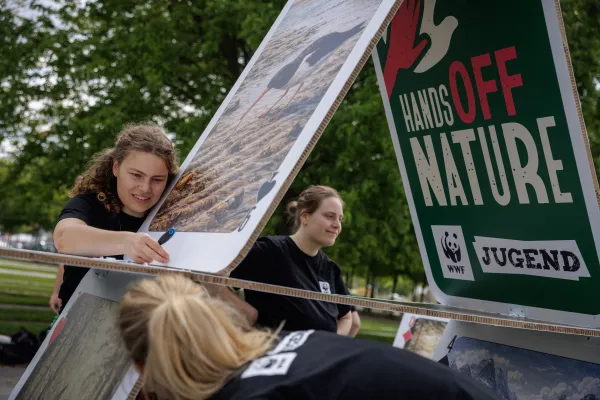 Mehrere junge Menschen der WWF Jugend bauen Kartenhaus der Biodiversität auf, um vor dem Kanzleramt für den Erhalt der EU-Naturschutzgesetze zu protestieren - Karten mit Naturmotiven und dem Slogan "Hands Off Nature" werden vorsichtig gestapelt.